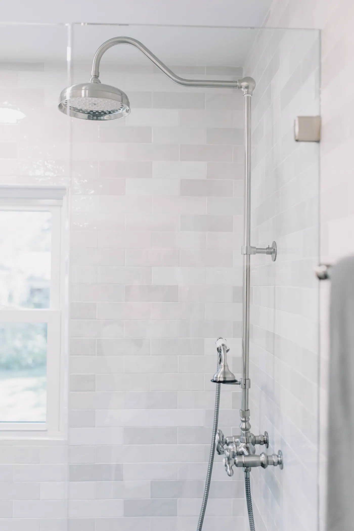 An exposed shower riser with a round rain head against pale subway tile in the Arlington Heights primary bath