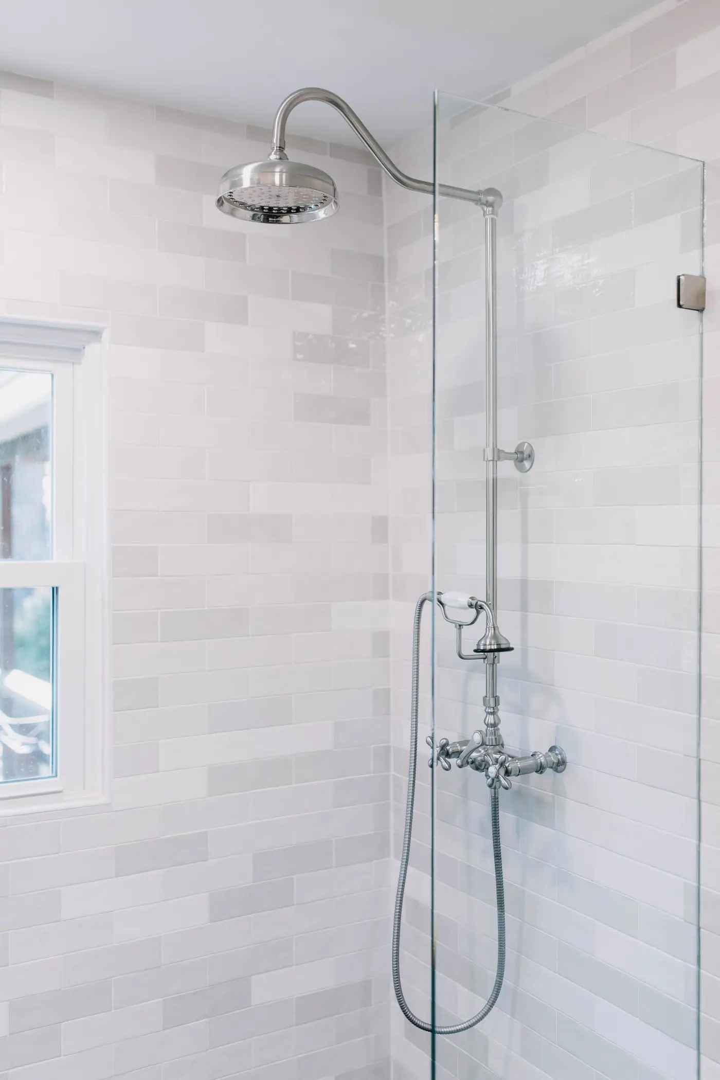 A handheld sprayer and rain head on one exposed riser beside the shower window in the Arlington Heights primary bath