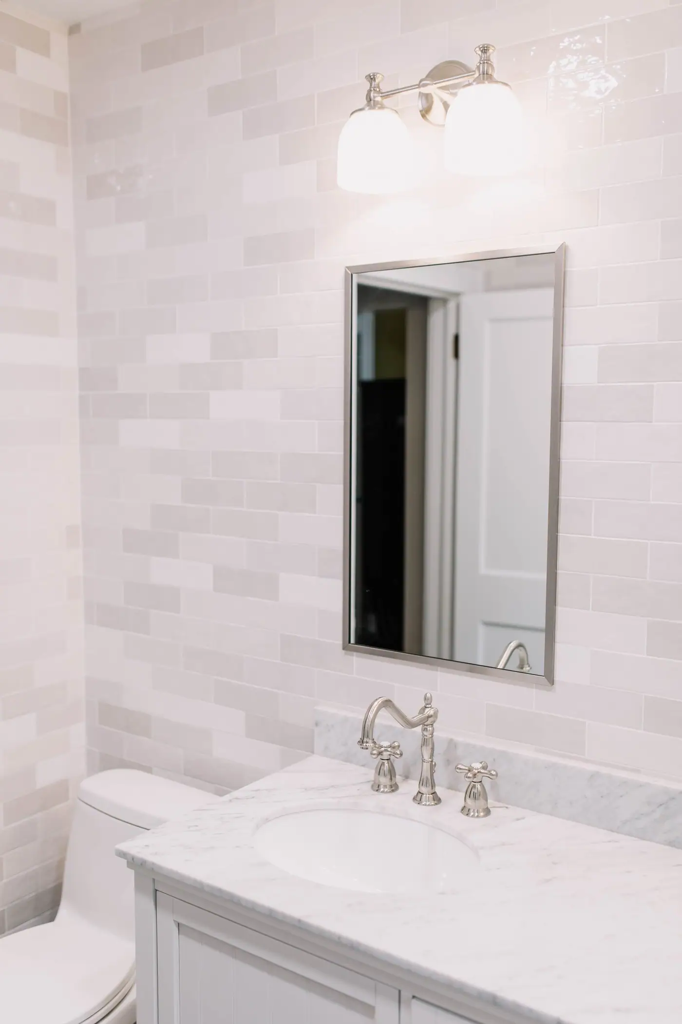 A single sink vanity with a veined top, a framed mirror, and a two-globe light beside the toilet in the Arlington Heights primary bath