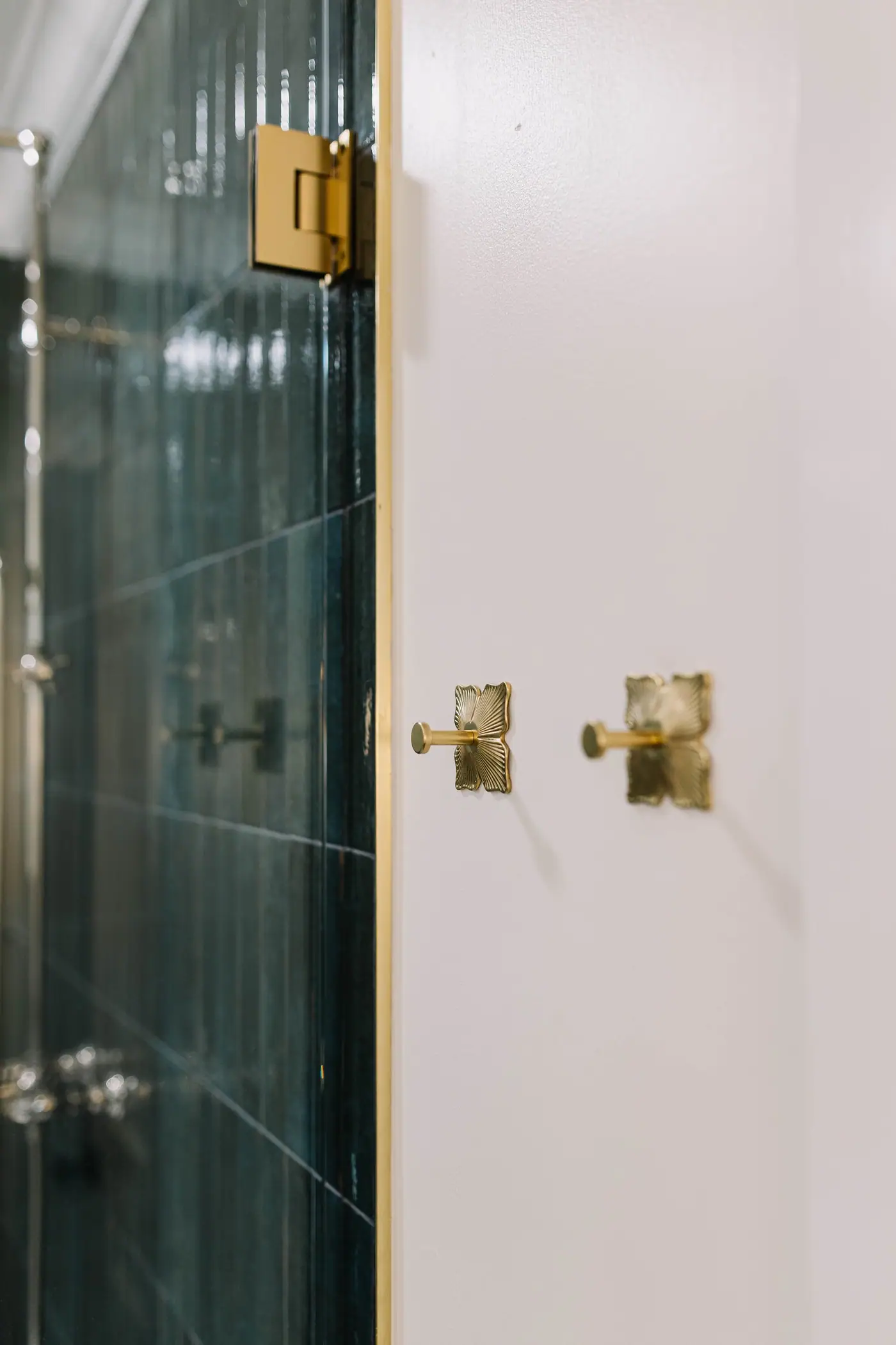 Brass shower door hinges and two brass fan-back robe hooks beside green stacked tile in the Berkeley Place bath design