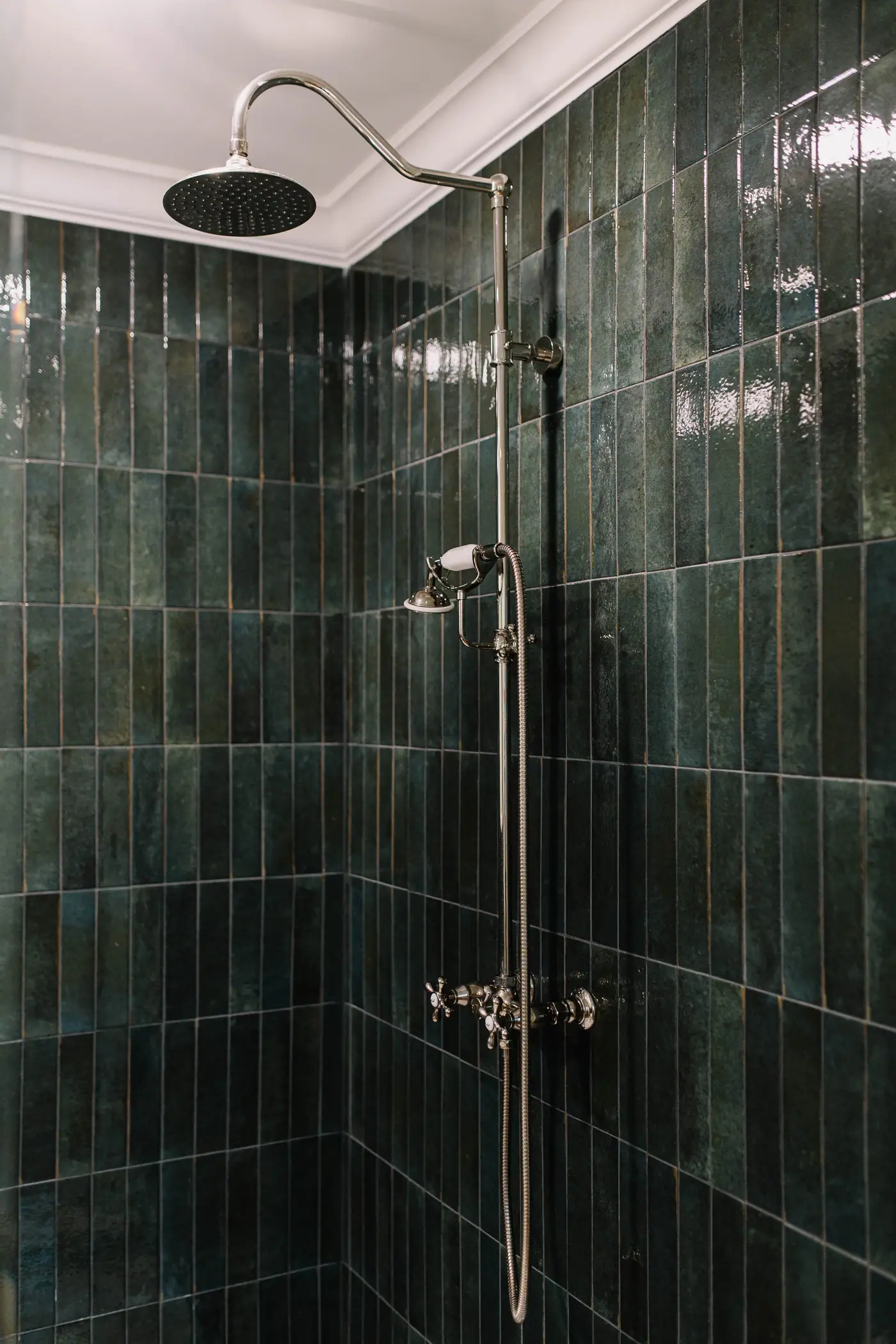 A deep green vertical tile shower with an exposed polished nickel rain shower and hand shower in a Berkeley Place bath design
