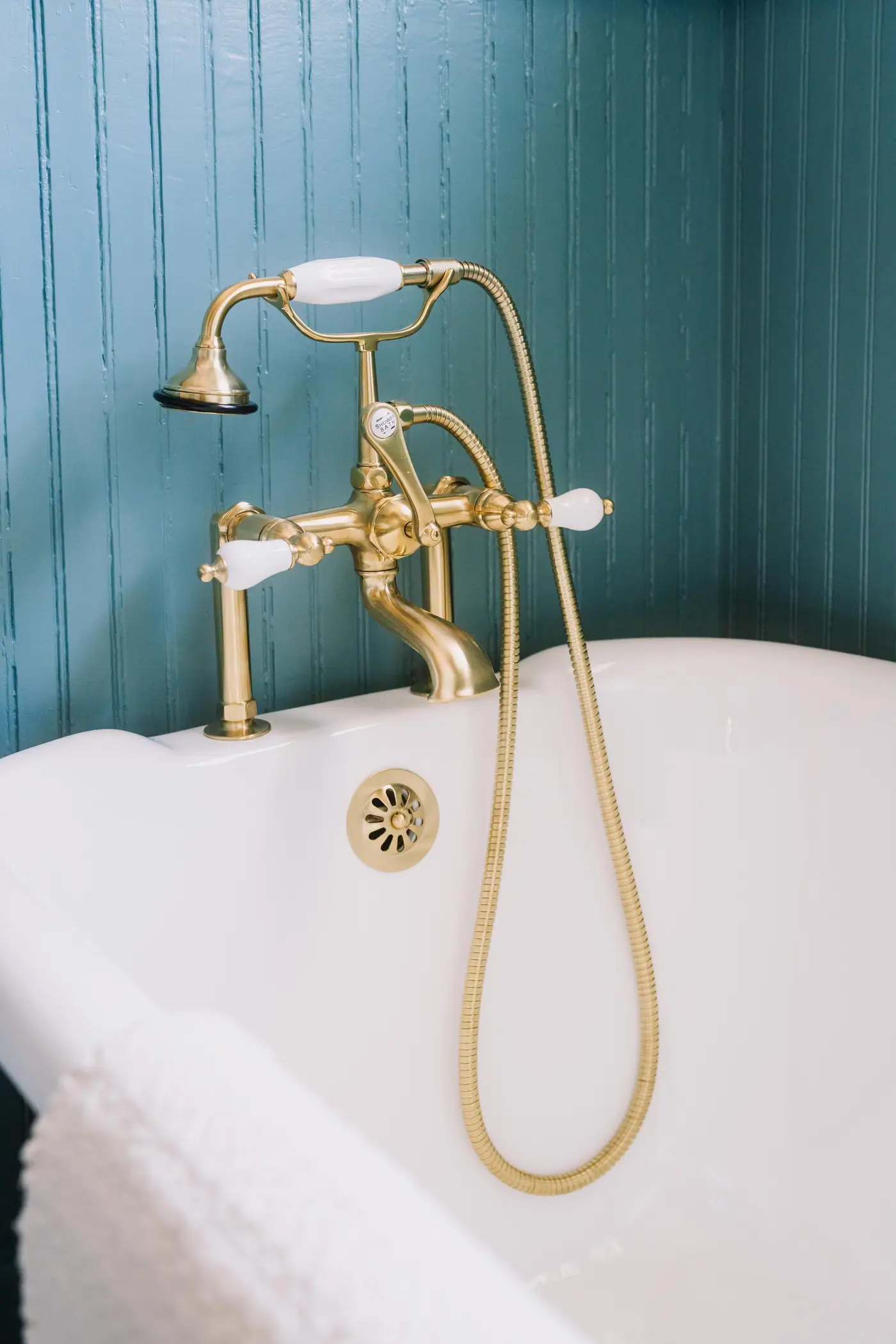 A brass tub filler and hand shower on a clawfoot tub against teal beadboard in a Fairmount guest bath remodel