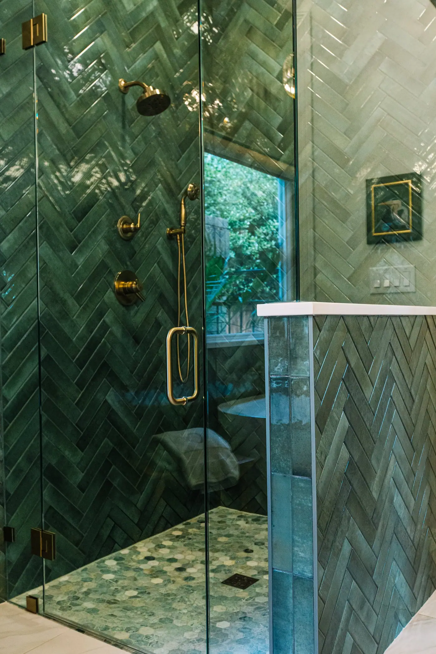A glass shower door with gold hinges, green herringbone walls, and a hexagon mosaic floor in the Mira Vista primary bath