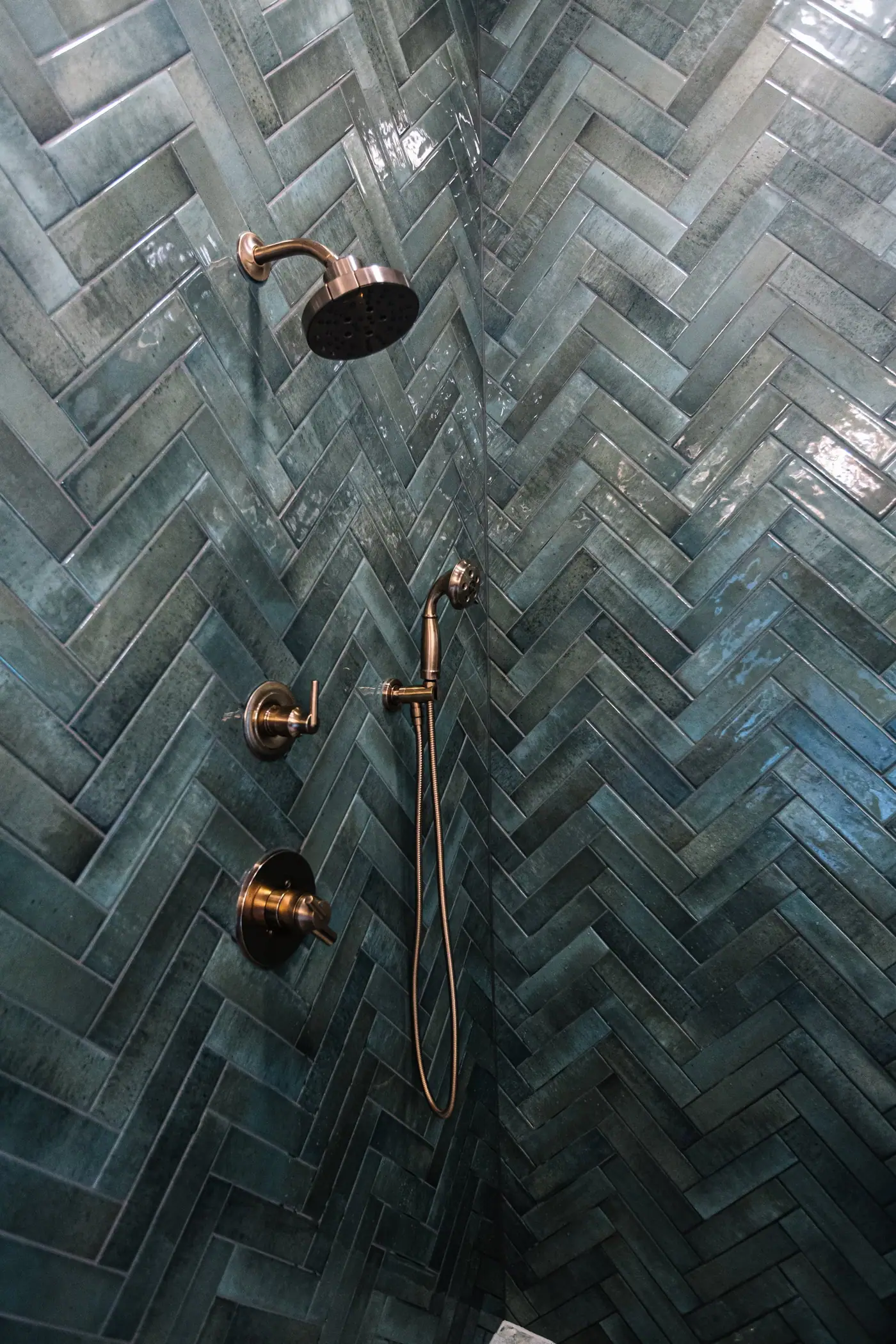 A shower head, handheld sprayer, and valves set into glossy green herringbone tile in the Mira Vista primary bath