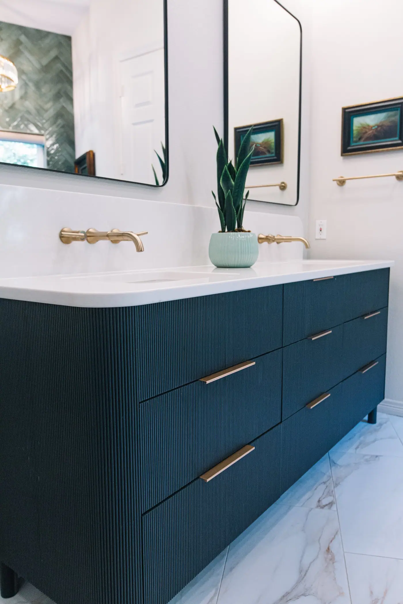 Gold bar pulls on a dark fluted vanity with rounded corners and legs above veined white floor tile in the Mira Vista primary bath