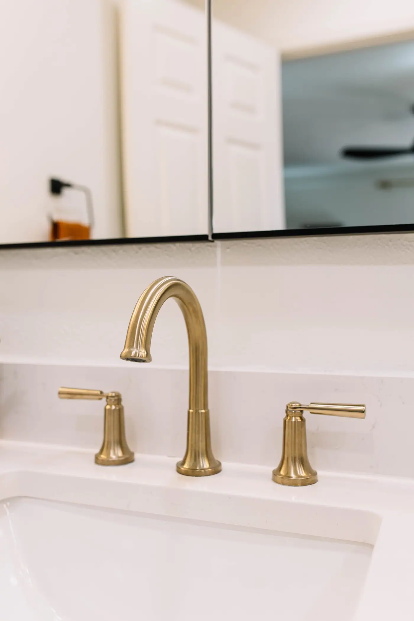 A champagne bronze faucet with lever handles on a white counter below the black-edged mirror in the Overton Park primary bath