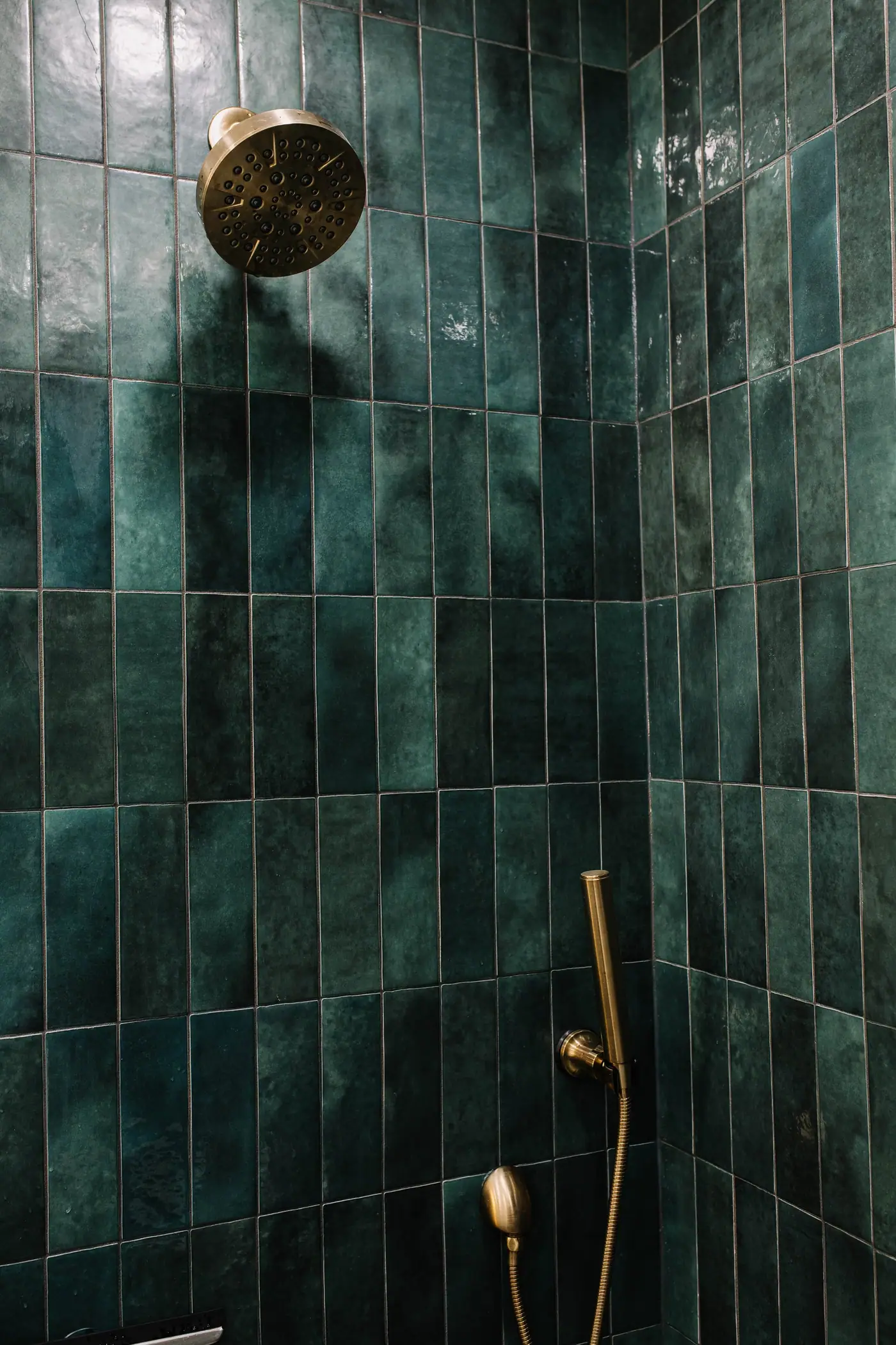 A champagne bronze shower head and handheld sprayer set against glossy, hand-glazed green tile in the Overton Park primary bath