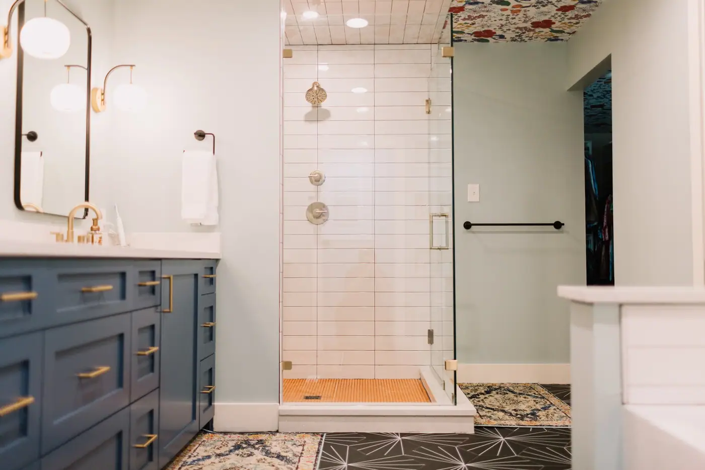 A white subway tile shower with a honey-toned floor and frameless glass beside the navy vanity in the Overton Park primary bath