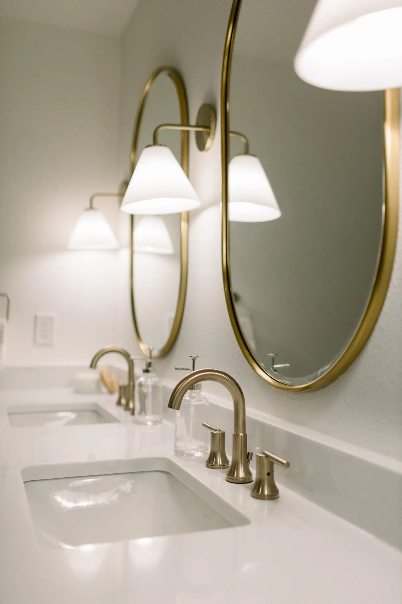 Twin oval brass mirrors and cone sconces over a double vanity with gold faucets in a Ridglea Hills primary bath