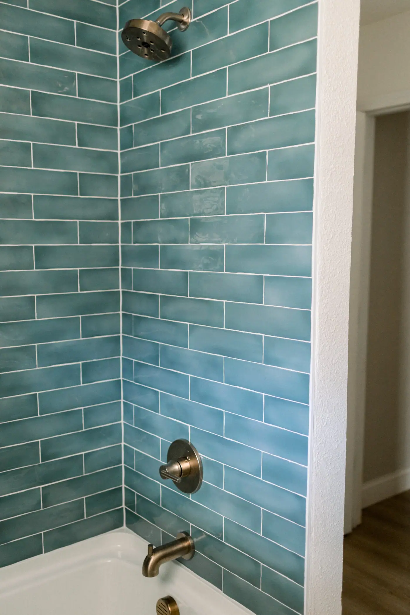 Teal glazed subway tile around a tub and shower, with a bronze-toned head, valve, and spout, in the Ridglea Hills bath