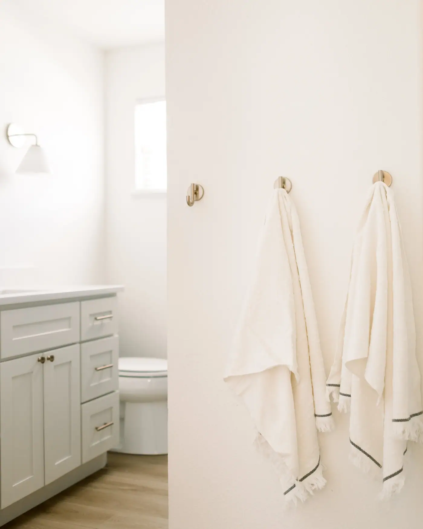 A light gray shaker vanity, toilet, and wood-look floor seen past towels on hooks in the Ridglea Hills secondary bath