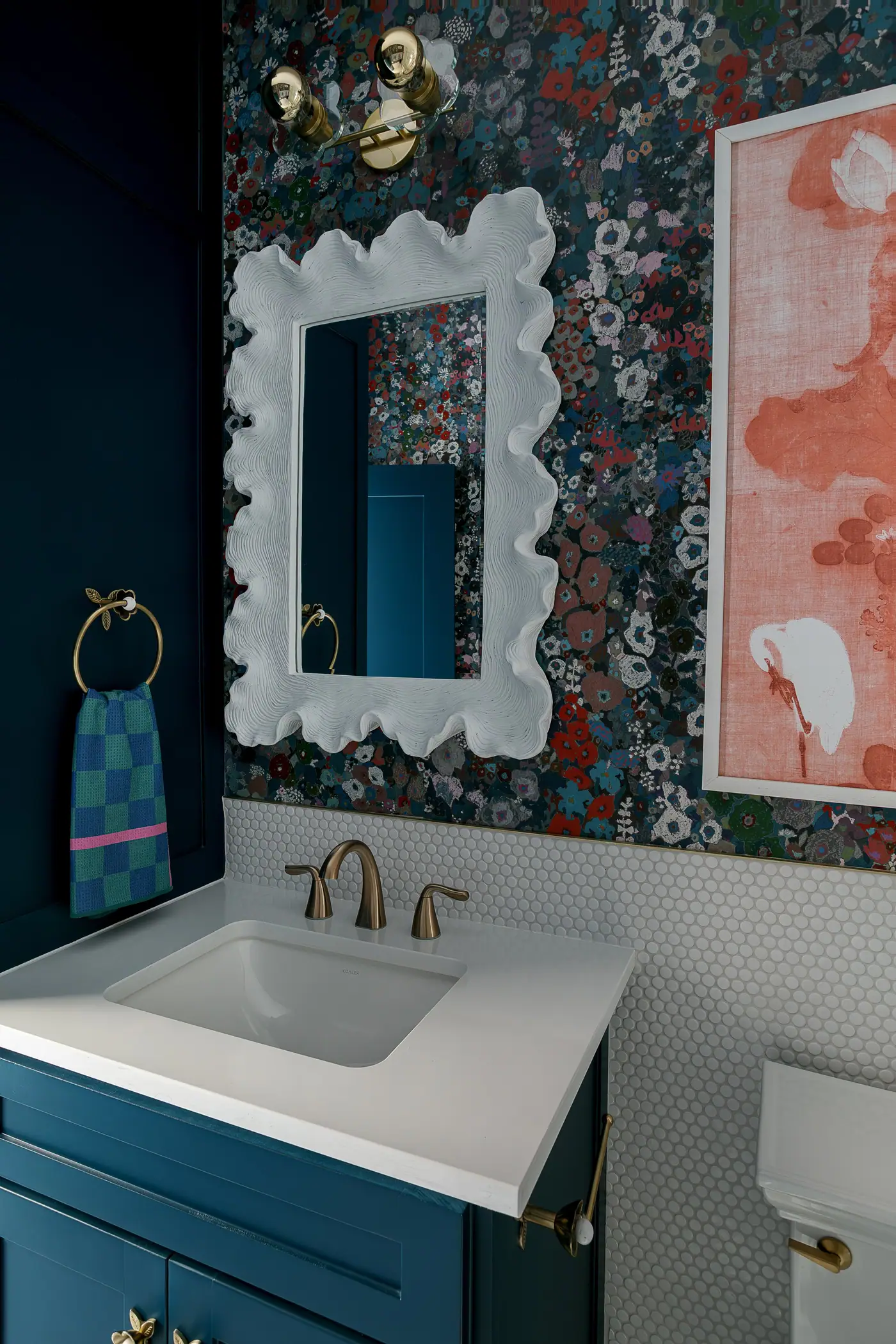 A navy vanity under a white scalloped mirror with dark floral wallpaper in a Westcliff bath