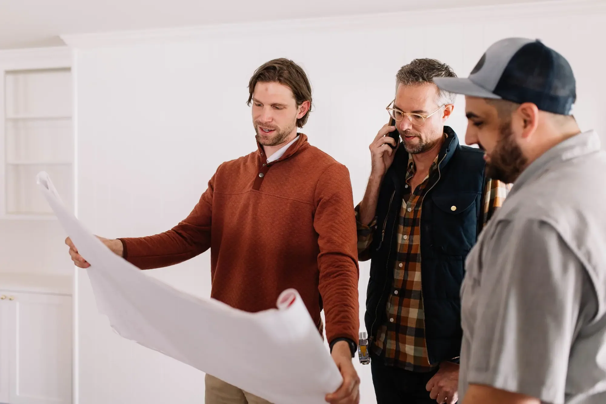 Three members of the 6th Avenue Homes construction team reading an unrolled floor plan inside a house under renovation