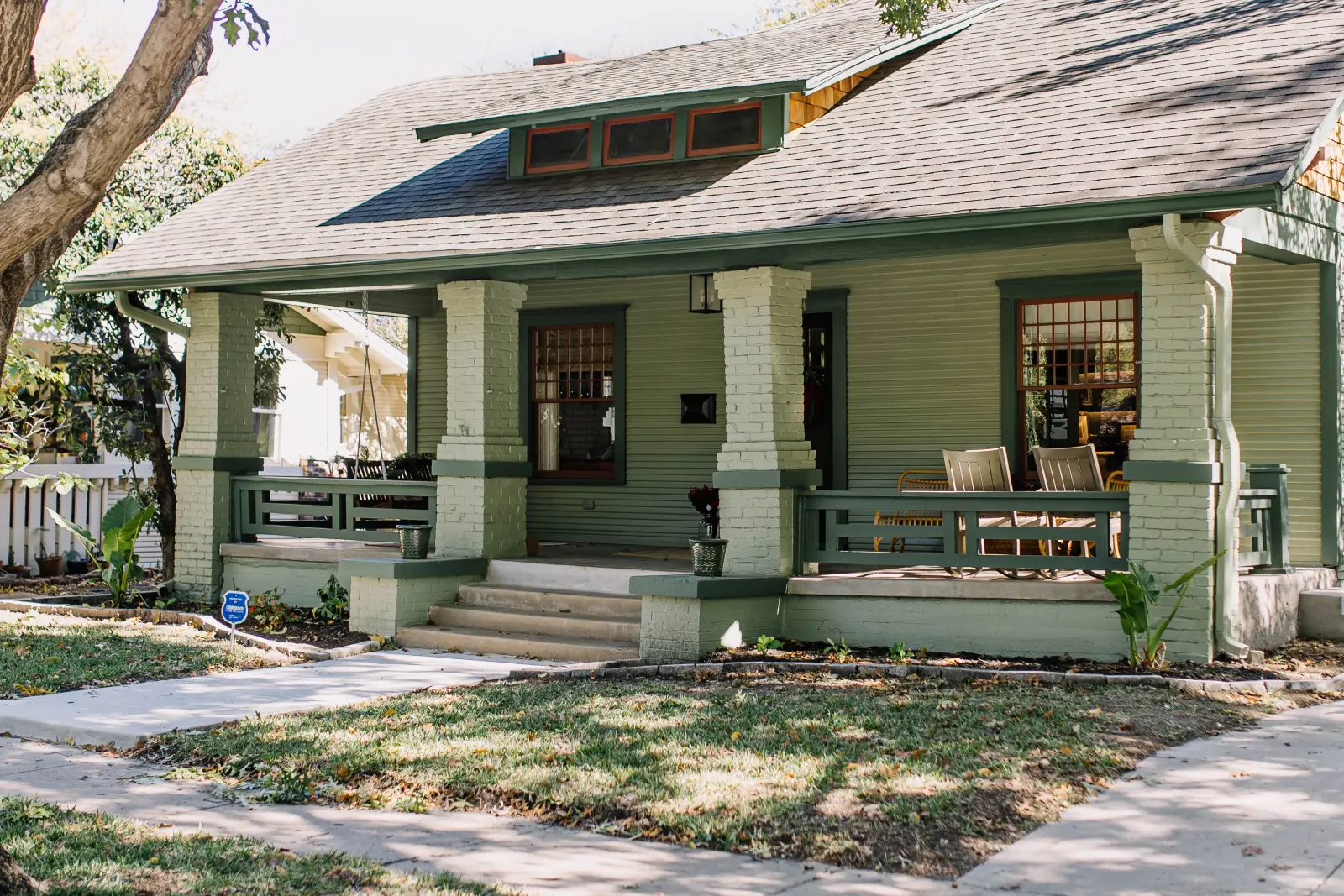 A green craftsman bungalow in Fort Worth with a deep front porch